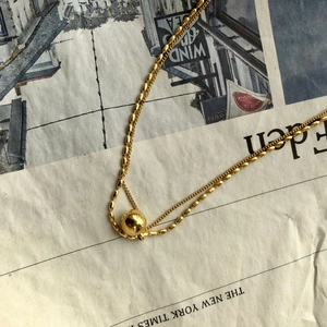 Detail view of a double-layer golden ball necklace on a vintage newspaper background