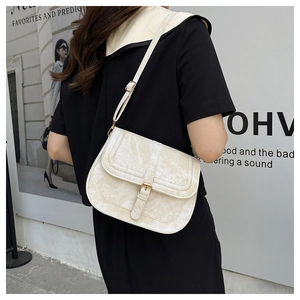 Street style shot of a cream saddle crossbody bag with vintage leather texture