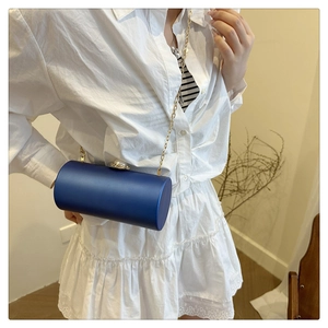 Détail d'un sac cylindrique en acrylique bleu avec fermoir perle et chaîne dorée sur modèle