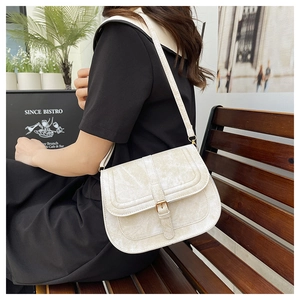 Close-up of vintage textured off-white saddle bag with golden hardware on a wooden bench