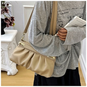 Detail of beige pleated leather shoulder bag with gold hardware worn on person