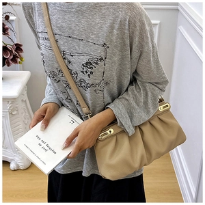 Detail of beige pleated leather shoulder bag with golden metallic clasp in a lifestyle setting