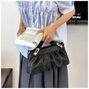 Detail of black pleated leather handbag with golden metal hardware in lifestyle setting
