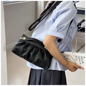 Detail of black pleated faux leather bag with lychee texture and gold metal buckle