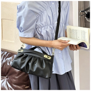 Detail of black pleated leather shoulder bag with gold hardware on a model