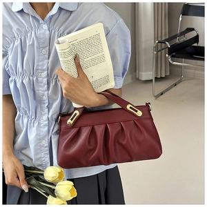 Detail of burgundy ruched handbag with lychee texture leather and gold metal buckles