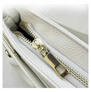 Detailed close-up of smooth gold zipper and lychee pattern leather on white handbag