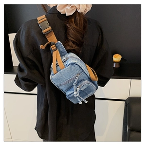 Detail der Brusttasche aus gewaschenem Denim mit Doppelreißverschluss und braunem Gurt