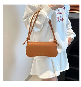 Close-up of tan leather shoulder bag featuring decorative knots and gold embossed logo