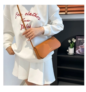Detailed close-up of brown textured leather crossbody bag with gold logo on fashion model
