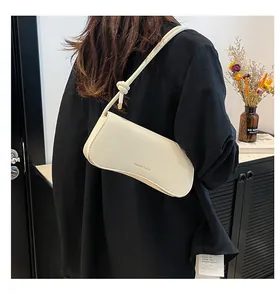 Detail of cream white leather shoulder bag with gold lettering and knotted strap design