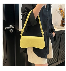 Detail of a bright yellow underarm bag featuring a curved base and knotted strap detail