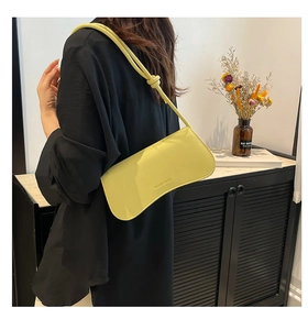 Detail showing bright yellow leather shoulder bag with knotted strap and minimalist text