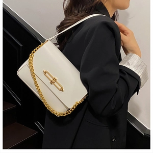 Detailed shot of white leather handbag featuring gold metal buckle and chunky chain strap