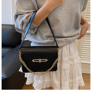 Detail of black leather shoulder bag with bold gold chain and metallic turn-lock closure