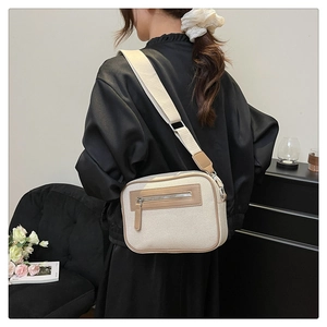 Borsa a tracolla in tela beige con tasca a zip, indossata in un ambiente interno