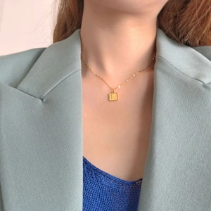 Détail d'un pendentif rose carré doré sur une chaîne délicate en acier titane pur