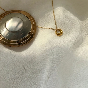 Elegant minimalist gold circle necklace on white linen background with artistic shadows