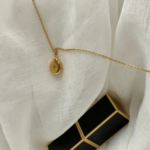Macro detail of gold teardrop necklace with star engraving on white linen fabric
