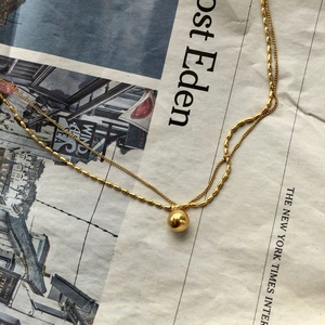 Double-layered gold ball pendant necklace featuring minimalist beads on a vintage newspaper background