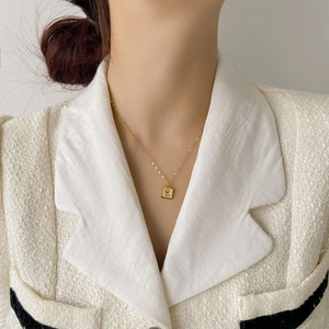 Détail d'un collier pendentif carré doré avec rose en relief porté par un mannequin