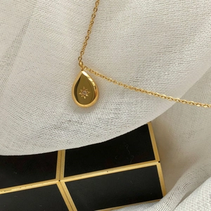 Close-up of golden teardrop pendant with star engraving and zircon on white mesh