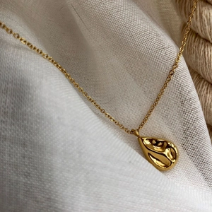 Collier à pendentif goutte d'eau dorée avec surface texturée sur fond de lin blanc cassé