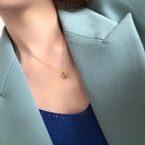 Close-up of minimalist gold circular pendant on a fine chain worn with a blue suit