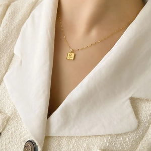 Gros plan d'un collier pendentif rose carré doré porté sur un blazer en tweed