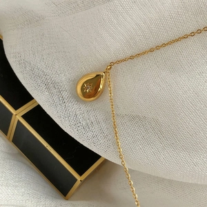 Close-up of golden teardrop pendant with starburst engraving and zircon on a gold chain
