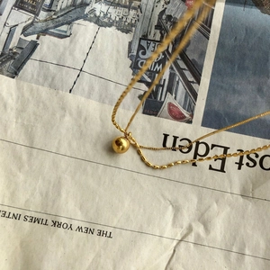 Double-layered gold ball pendant necklace displayed on a vintage newspaper background