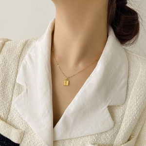 Détail du collier doré avec pendentif carré rose gravé porté par un mannequin chic