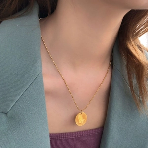 Close-up of gold coin necklace with praying hands and One Day at a Time engraving