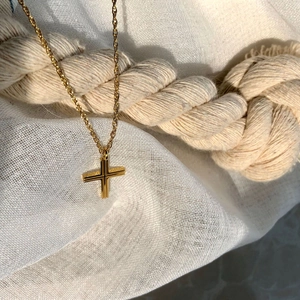 Close-up of golden cross necklace with textured surface on a rustic rope background