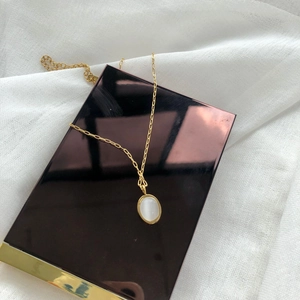 Macro shot of oval white gemstone pendant on a gold chain against a textile texture