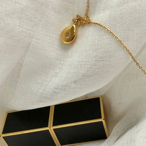 Close-up of gold titanium necklace with star-engraved water drop pendant and zircon