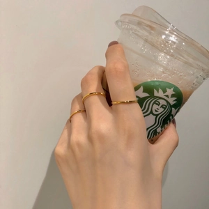 Close-up of three minimalist thin gold stacking rings worn while holding a coffee cup