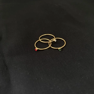 Detailed close-up of three 14k gold-plated rings with red, green, and white gemstones