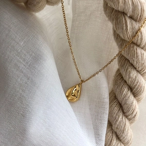 Collier à pendentif goutte dorée avec texture de métal liquide sur fond de tissu blanc