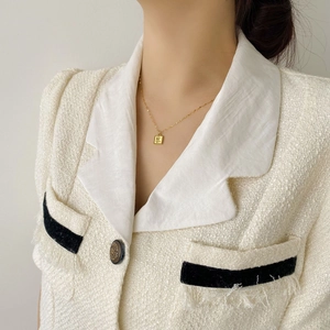 Collier doré avec pendentif carré rose porté sur une veste en tweed blanc chic