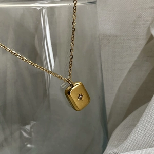 Macro shot of rectangular gold starburst pendant with crystal on minimalist chain