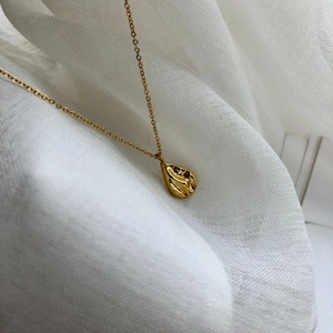 Vue détaillée d'un pendentif goutte d'eau dorée texturée sur un tissu en lin blanc