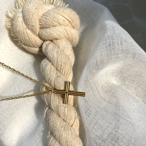 Minimalist double-layered gold cross necklace on textured fabric background