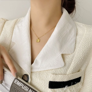 Détail d'un collier pendentif rose carrée en acier titane porté par un mannequin