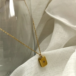 Detail of gold titanium steel necklace with rectangular star engraved pendant and rhinestone