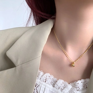 Detail of a minimalist gold beaded necklace worn over a green blazer and lace top