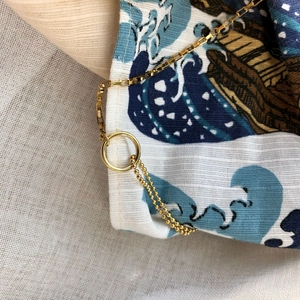 Minimalist gold asymmetric chain necklace with smooth ring on blue wave pattern fabric