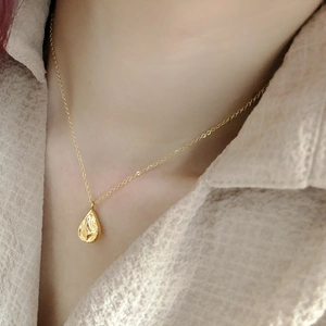 Gros plan d'un collier avec pendentif goutte d'eau dorée à texture lave porté par un modèle
