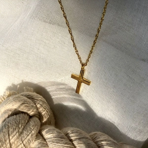 Detailed close-up of a gold cross pendant featuring elegant vertical stripes and a fine chain
