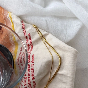 Close-up of polished gold snake bone chain bracelet resting on soft white textured fabric